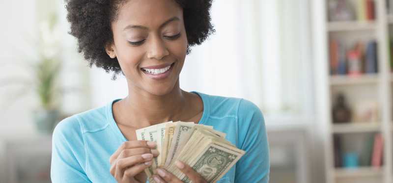 Smiling adult holds dollar bills in hand, fanned out.
