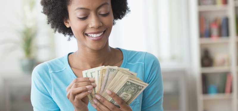 Smiling adult holds dollar bills in hand, fanned out.
