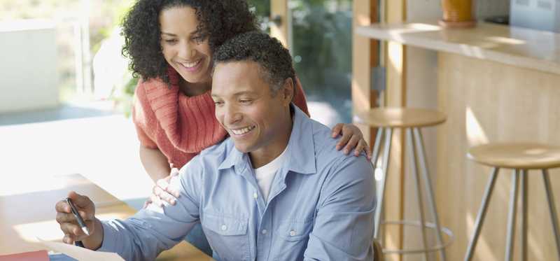 Two adults smile as they review paperwork at kitchen table.
