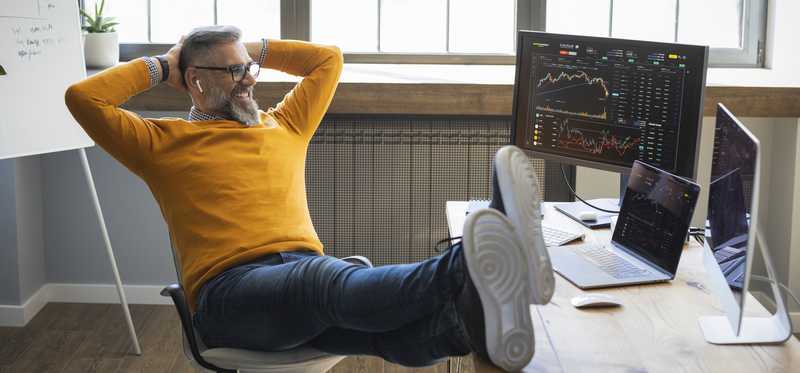 Person leaning back in chair with hands behind their head and looking at computer screen.