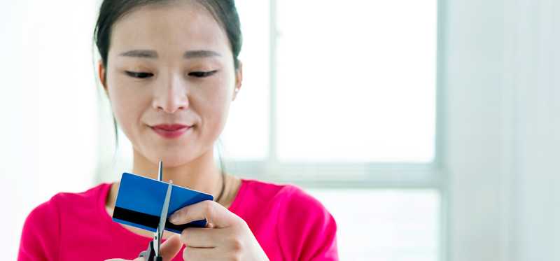 Person wearing pink shirt cuts credit card with scissors.