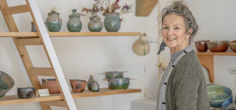 Person standing and smiling in pottery shop.