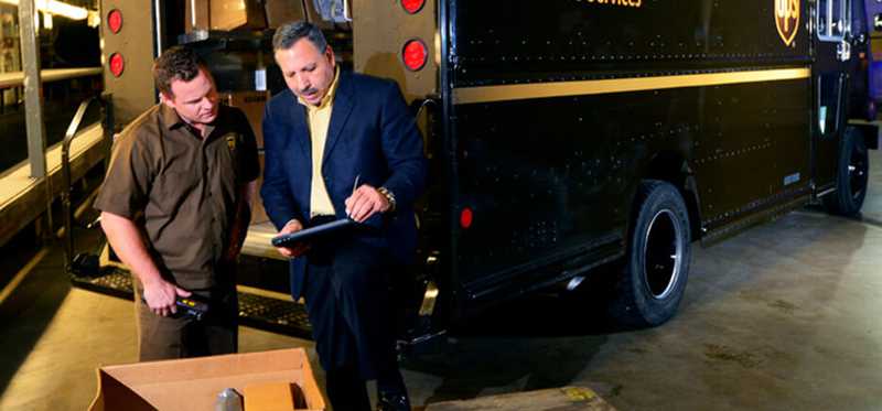 Two people standing outside a UPS delivery truck full of boxes.