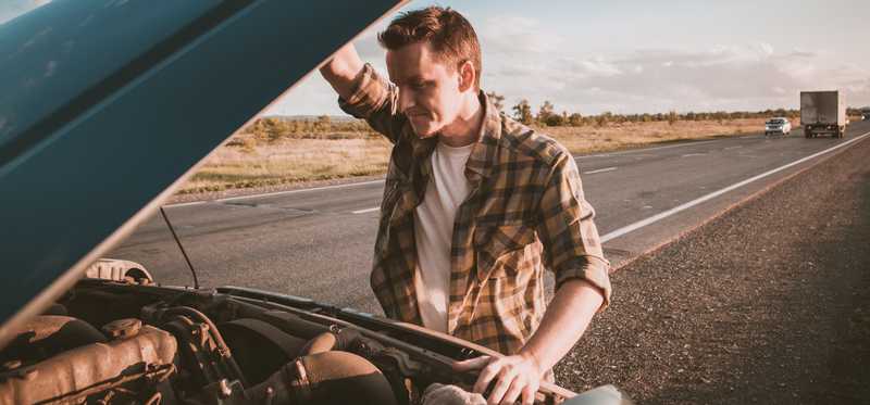 Young man looks under the hood of his car.