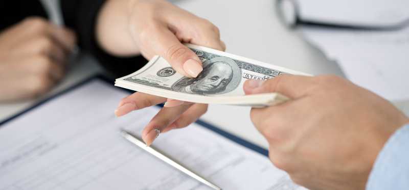 One hand passing a wad of money across a desk to another hand.