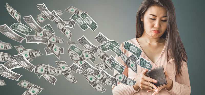 Person looking into open wallet as dollars fly out.