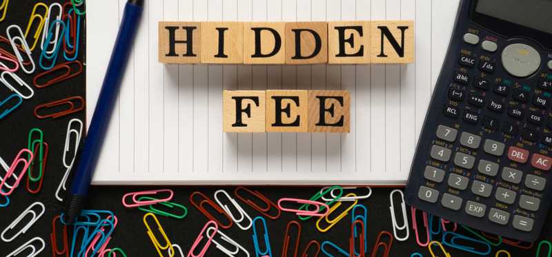 Wooden blocks spelling out Hidden Fee with pen, calculator, notebook, and paper clips nearby