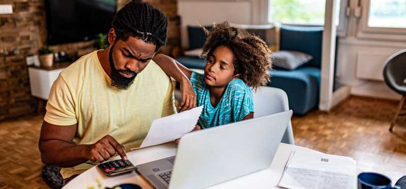 Child watches man looking at paper and using calculator.