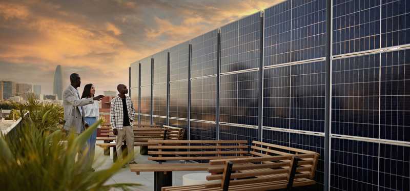 Three people looking at a wall of solar panels.