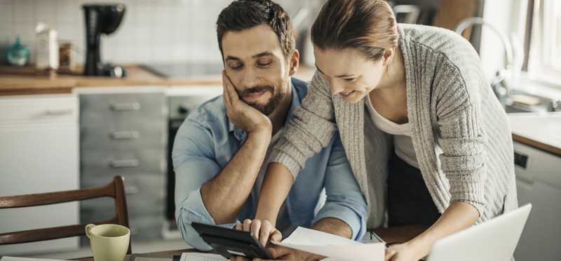Two people working on calculator and paperwork in kitchen.