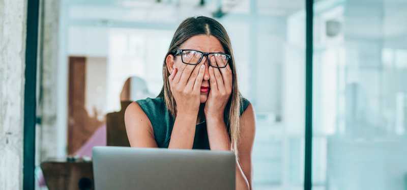 Woman covering face with her hands as she sits at laptop in office