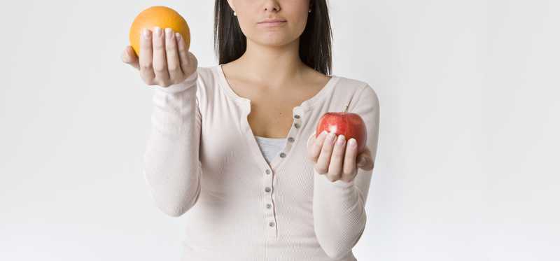 Woman holding apple in one hand and orange in other
