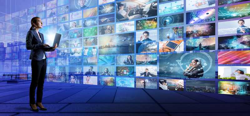 Woman with laptop in front of numerous video screens
