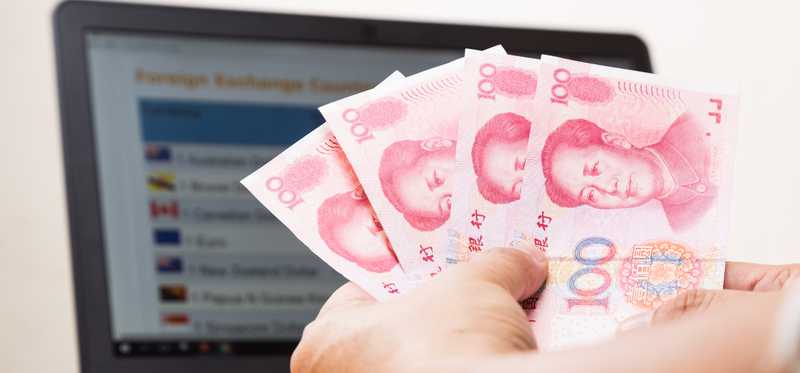 Hand holding 100 yuan notes in front of laptop