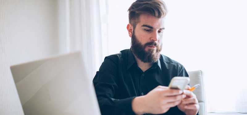 Person holding phone while sitting at desk with open laptop.