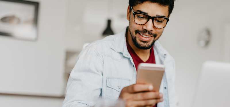 Person looks at phone while using laptop.