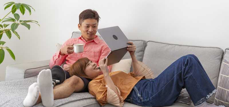 Two smiling adults on couch look at laptop screen.