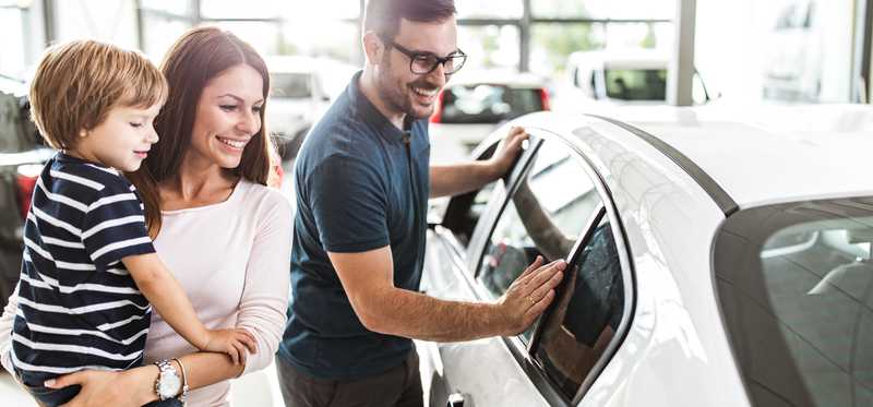 Two people with child look at new car in dealership.