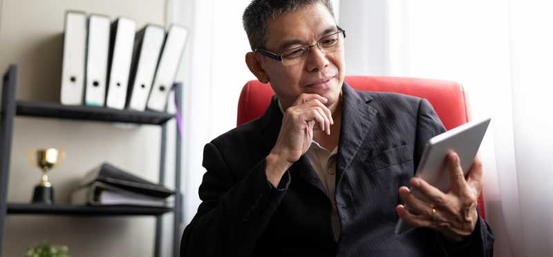 Adult in professional attire smiles while looking at tablet.