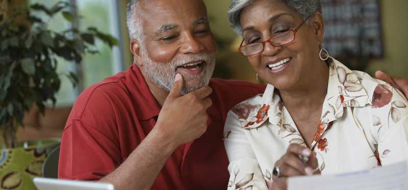 Two people smiling while looking at paperwork at home.