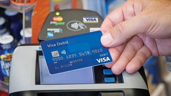 Hand holding a blue Visa card in front of a POS device.