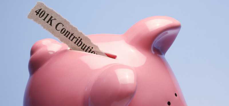 Slip of paper saying 401k Contribution being slipped into piggy bank.