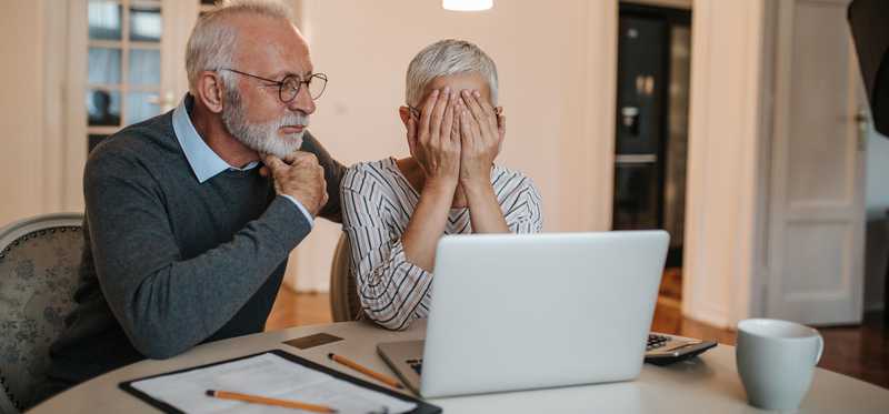 Two people look at a laptop screen with one covering their face.