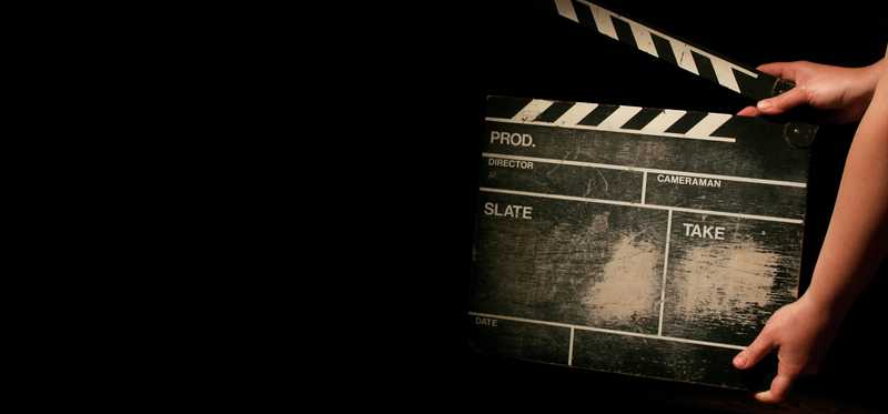Movie clapboard being held against a dark background.