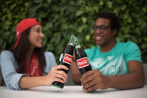 A young adult male and female enjoying bottles of Coke together.