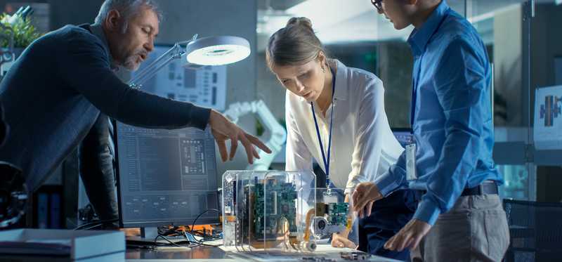 Three people leaning over and working on a model that sits on a desk in a technology lab.