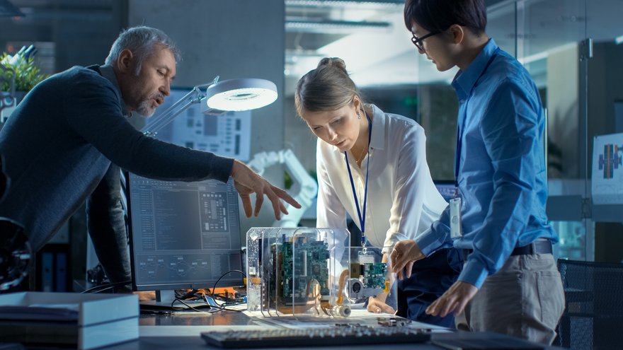 Three people leaning over and working on a model that sits on a desk in a technology lab.
