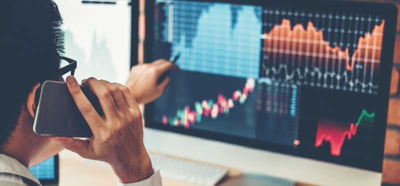 Investor talking on phone and looking at stocks on computer.