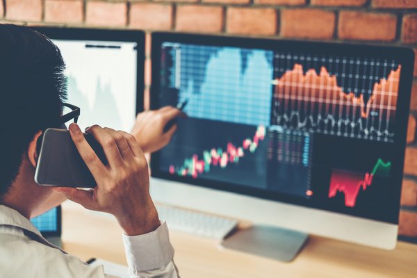 Investor talking on phone and looking at stocks on computer.