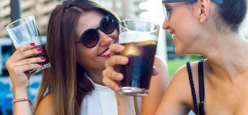 Two peole drinking glasses of soda.