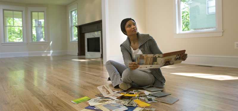 Person sitting on the floor in an empty home and looking at paint swatches for the interior walls.