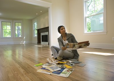 Person sitting on the floor in an empty home and looking at paint swatches for the interior walls.