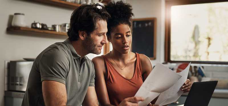 Two people reviewing paperwork while sitting at table with laptop.