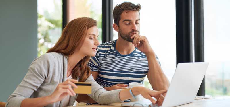 Two people looking at laptop while one points and holds credit card.
