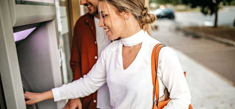 Person smiles while using ATM machine outside.