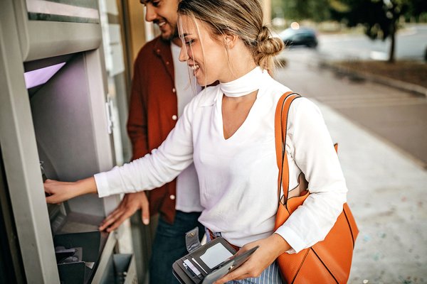 Person smiles while using ATM machine outside.