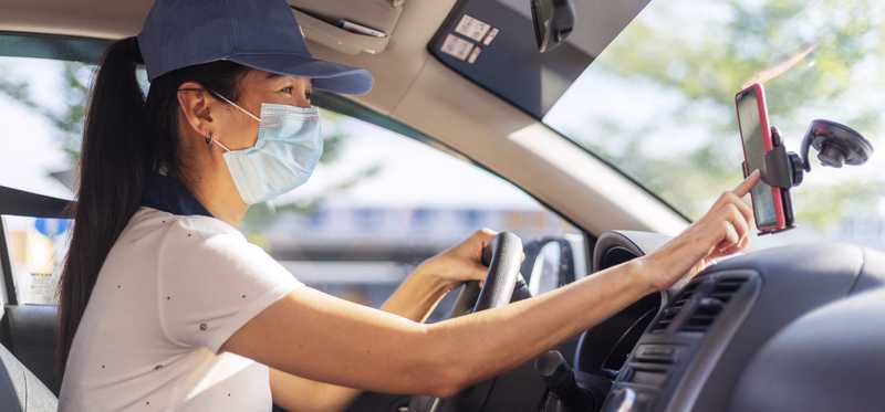 Masked driver touching smartphone.