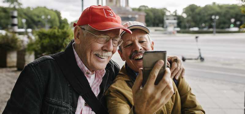 Two happy people look at phone while outdoors.