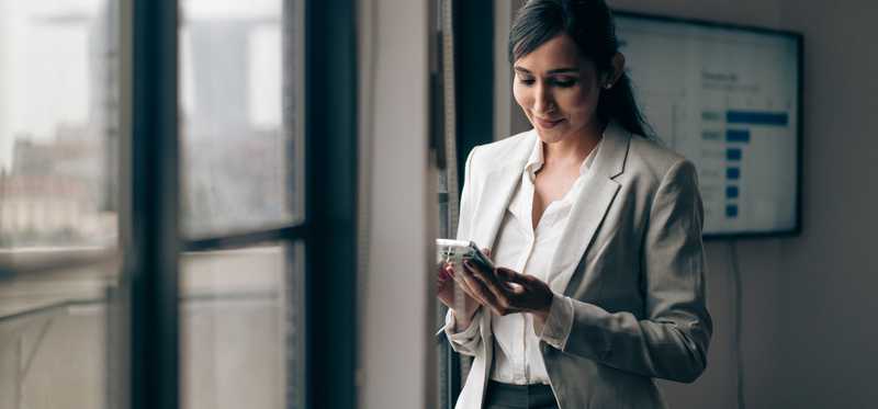 Person looks at phone and smiles while standing next to office window.