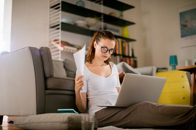 Person sitting on couch with laptop and paperwork.