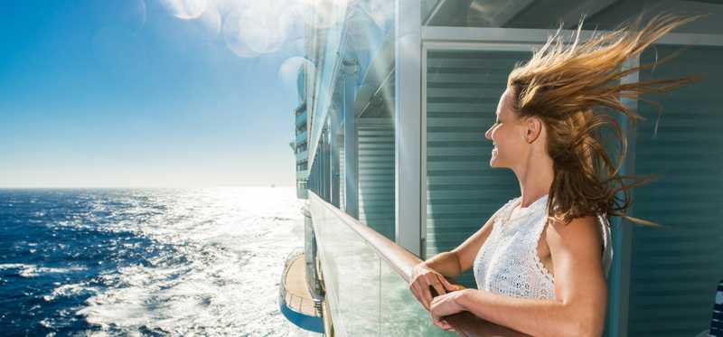 A wind-swept person looking at the ocean from a deck of a cruise ship.