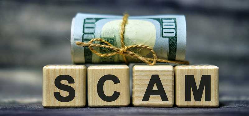 Roll of 100-dollar bills on blocks that spell Scam.