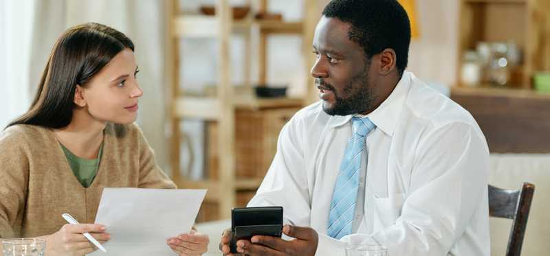 Two people sit at table with calculator and paperwork.