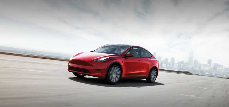 Red Tesla Y electric vehicle on an empty road outside a city