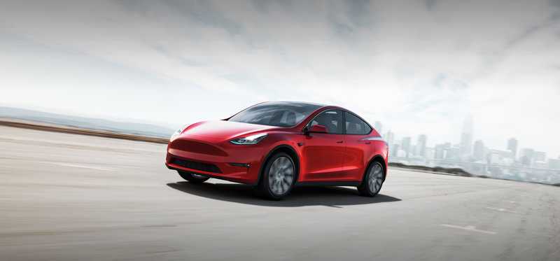 Red Tesla Y electric vehicle on an empty road outside a city.