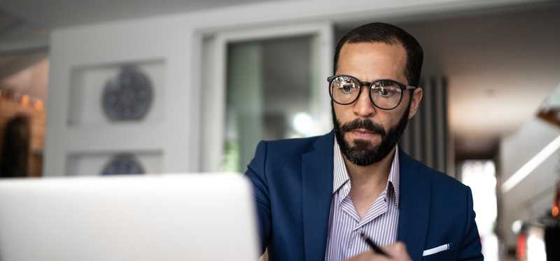 Professionally dressed individual takes notes in front of laptop.